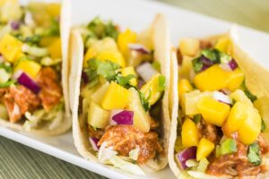 Corn tortillas filled with shredded lettuce, shredded barbecue chicken and topped with mango pineapple salsa