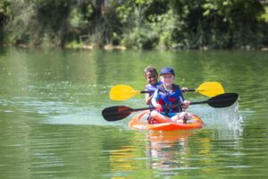 Two cute diverse young boys kayaking down a beautiful river. Smiling and having fun together on a warm day at summer camp